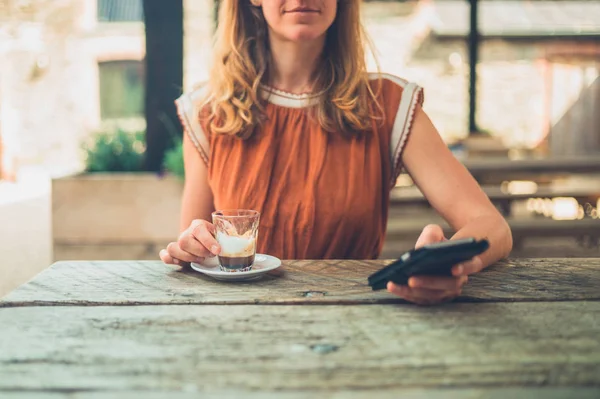 若い女性はエスプレッソを飲んで 外のテーブルで彼女のスマート フォンを使用して — ストック写真