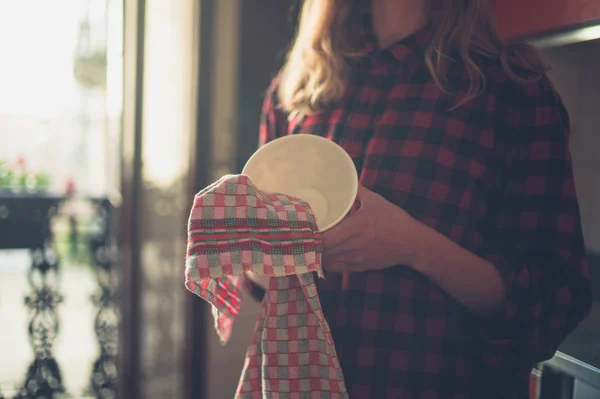 一个年轻的女人正在擦她厨房里的盘子 — 图库照片