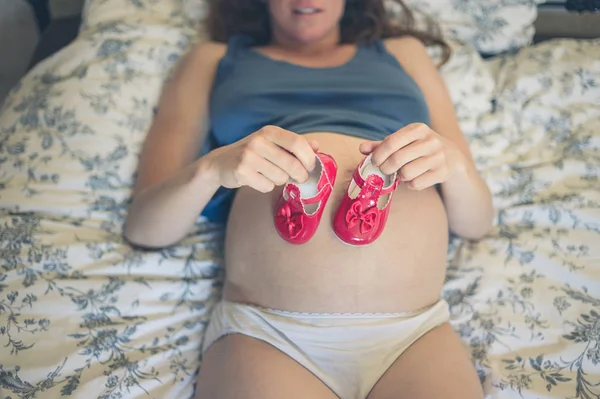 Una Joven Embarazada Está Acostada Cama Casa Con Zapatos Bebé — Foto de Stock