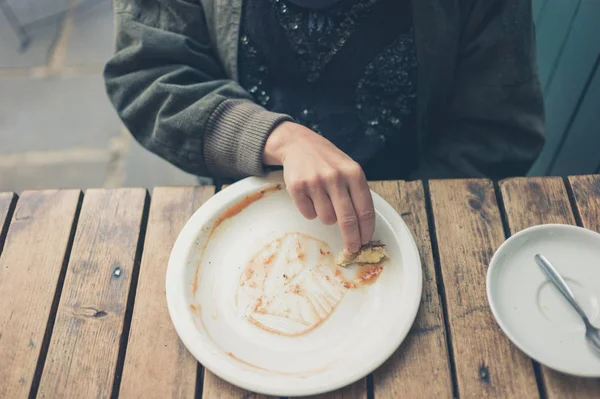 一个年轻的女人正在用一块面包把盘子里的酱汁擦掉 — 图库照片
