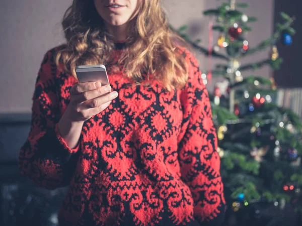 一位年轻女子在圣诞树旁使用智能手机 — 图库照片