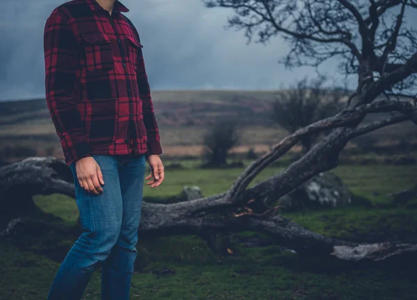 一个年轻人站在荒原上倒下的树旁边 — 图库照片