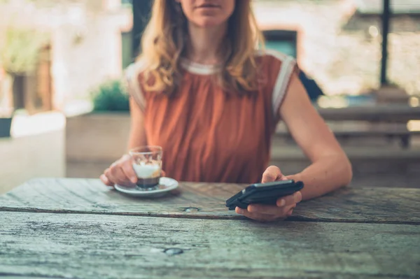 若い女性はエスプレッソを飲んで 外のテーブルで彼女のスマート フォンを使用して — ストック写真