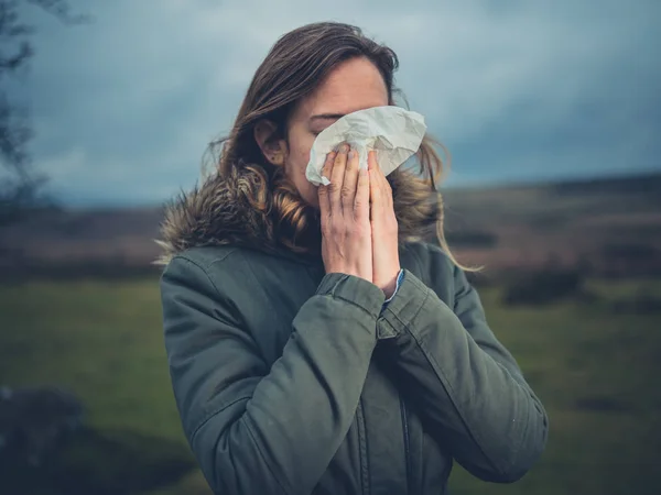 A young woman is blowing her nose on the moor