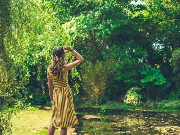 ドレスを着ているおしゃれな女性の後姿が庭の池に立っています — ストック写真