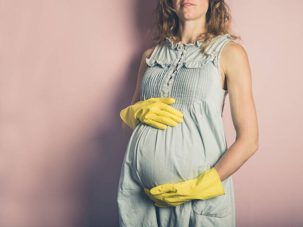 A young pregnant woman is wearing yellow rubber gloves