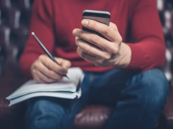 Uomo Seduto Divano Usando Uno Smartphone Scrivendo Quaderno — Foto Stock