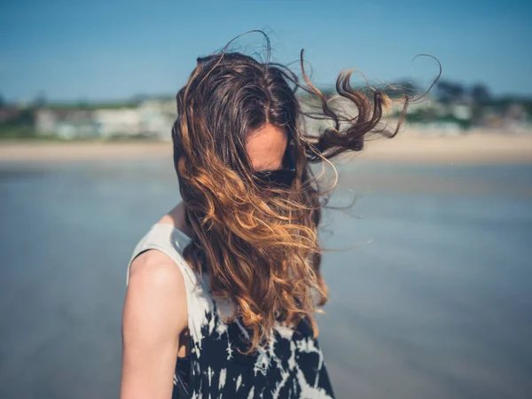 若い女性が髪を風になびかせ ビーチに立っています — ストック写真