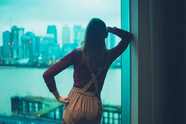 一位年轻女子在城市公寓里 正在看外面的摩天大楼 — 图库照片