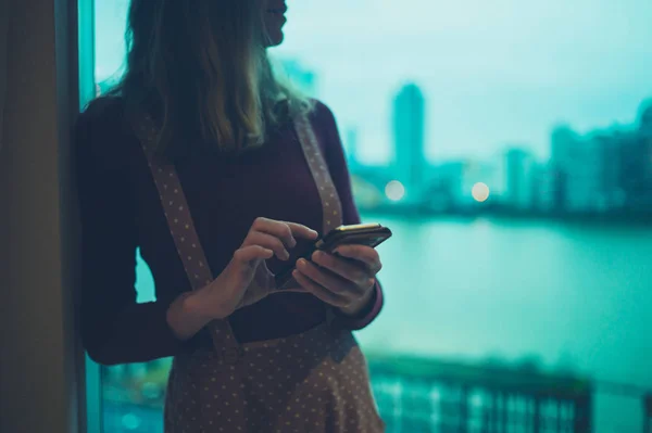 Ung Kvinna Använder Sin Smartphone Genom Fönstret Stadslägenhet — Stockfoto