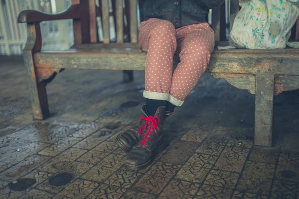 一个穿着靴子的年轻女人坐在户外的长凳上的脚 — 图库照片