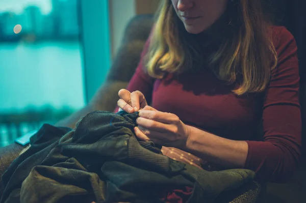 一个年轻的女人正在城市公寓的窗户旁缝制衣服 — 图库照片