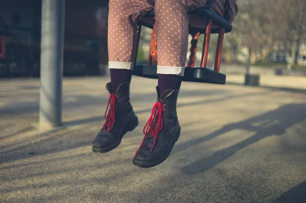 一个穿着靴子的年轻女子坐在公园的秋千上 — 图库照片