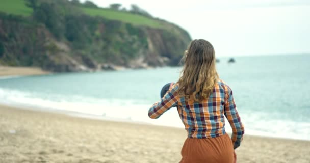 Mujer joven en la playa lanzando y atrapando una pelota — Vídeo de stock