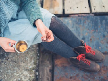 Genç bir kadın açık havada çay içme ve yeme çikolata oturuyor