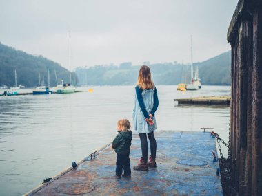 Genç bir anne ve onu yürümeye başlayan bir eski paslı iskelede duran