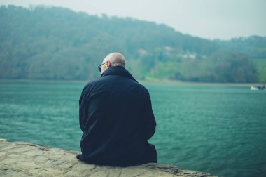arka planda dağ ile nehir tarafından oturan kıdemli adam