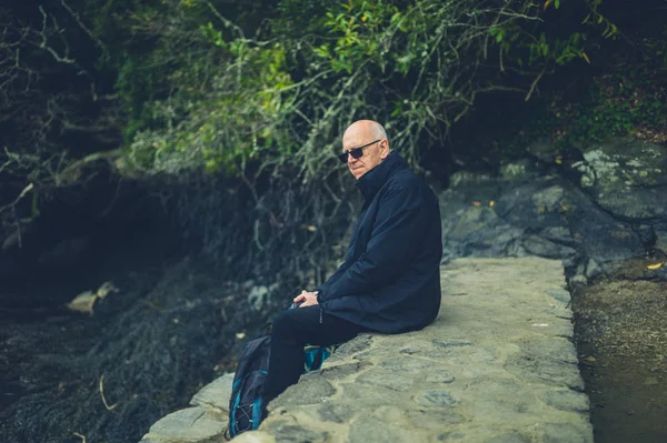 Starszy Mężczyzna Okularów Słonecznych Siedzi Zewnątrz Kamienia Ogrodzenia — Zdjęcie stockowe