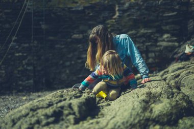 Genç bir anne ve onun yürümeye başlayan bir plajda kayalar keşfetmek