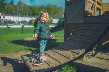 Küçük bir bebek oyun alanında oyun ekipmanları üzerinde yalınayak duruyor