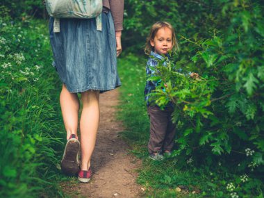 Kibar bir küçük çocuk, annesi geçebilsin diye doğa yolundaki çalıları temizliyor.
