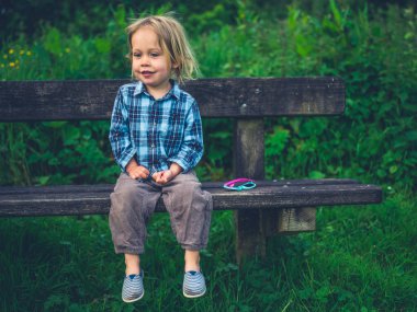 Küçük bir bebek bir bankta oturuyor ve doğada rahatlatıcı