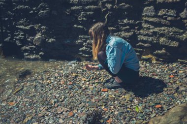 Genç bir kadın güneşli bir yaz gününde sahilde bir şeyler topluyor.