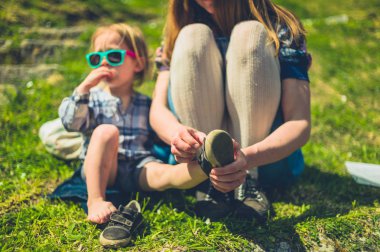 Genç bir anne, güneşli bir yaz gününde parkta ayakkabılarını giymesine yardım ediyor.