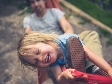 Küçük bir çocuk babasıyla bir hamakta eğleniyor.