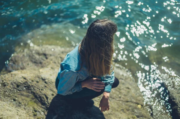 若い女性は 夏の晴れた日に水のそばの岩の上でリラックスしています — ストック写真