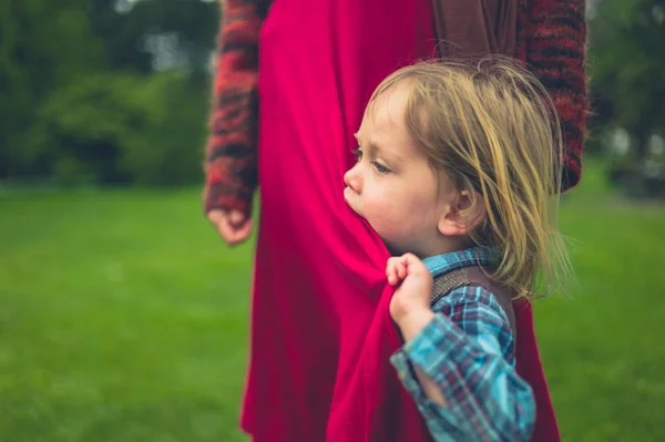 유아는 공원에서 잔디밭에 어머니에 집착하고 그녀의 드레스를 입고있다 — 스톡 사진
