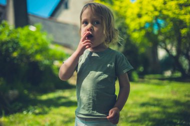 Küçük bir çocuk bir yaz gününde bir parkta çimüzerinde duruyor