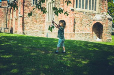 Küçük bir çocuk parkta bir ağaç dalı ile oynuyor