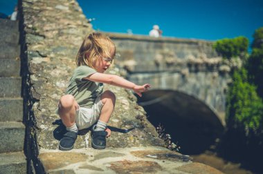 Küçük bir bebek yaz aylarında bir köprünün yanındaki taş duvarda oturuyor.