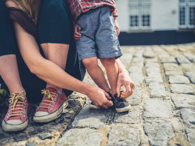 Genç bir anne, arnavut kaldırımlı bir sokakta ayakkabılarını açık havada ona bebek yardımcı oluyor