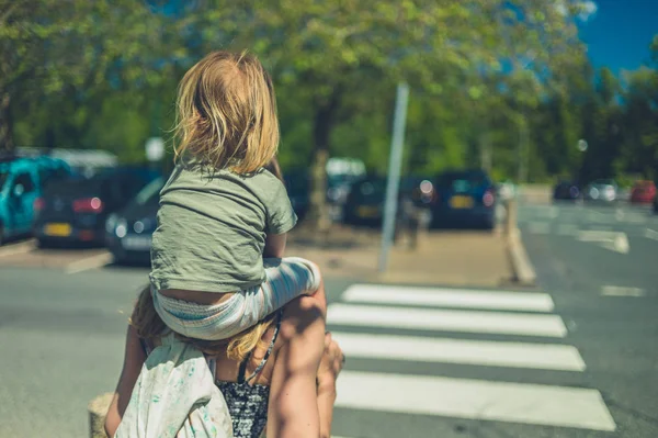 小さな幼児は 日当わりの夏の日に駐車場で彼の母親の肩に乗っています — ストック写真
