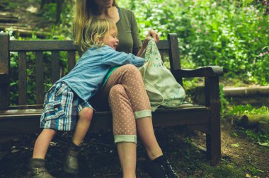 Küçük bir çocuk annesinin çantasından bir şey alıyor.