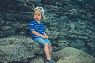 Küçük bir bebek bir yaz gününde küçük bir kasabada bir taş duvarın yanında oturuyor