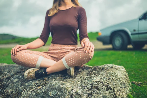 年轻女子坐在冥想在岩石附近的汽车在自然 — 图库照片