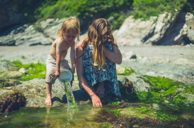 Küçük bir bebek annesi ile sahilde ve bir kova su sıçrayan olduğunu