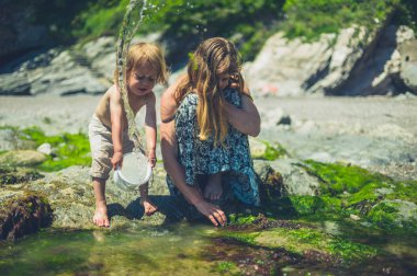 Küçük bir bebek annesi ile sahilde ve bir kova su sıçrayan olduğunu