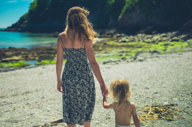 Genç bir anne güneşli bir yaz gününde sahilde onu bebek ile el ele yürüyor