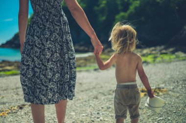 Genç bir anne güneşli bir yaz gününde sahilde onu bebek ile el ele yürüyor