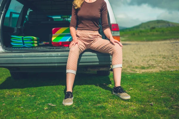 若い女性は 晴れた夏の日に自然の中で彼女のステーションワゴンの後ろに座っています — ストック写真