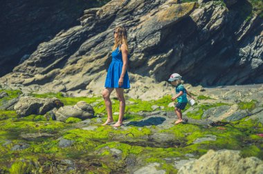 Genç bir anne güneşli bir yaz gününde onu bebek ile kayalık bir plajda yürüyor