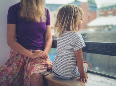 Genç bir anne ve onun küçük yürümeye başlayan bir şehir dairenin penceresinden dışarı bakıyor