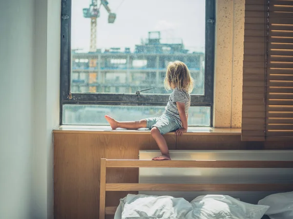 Little toddler sitting by the window in city aparetment — Stock Photo, Image