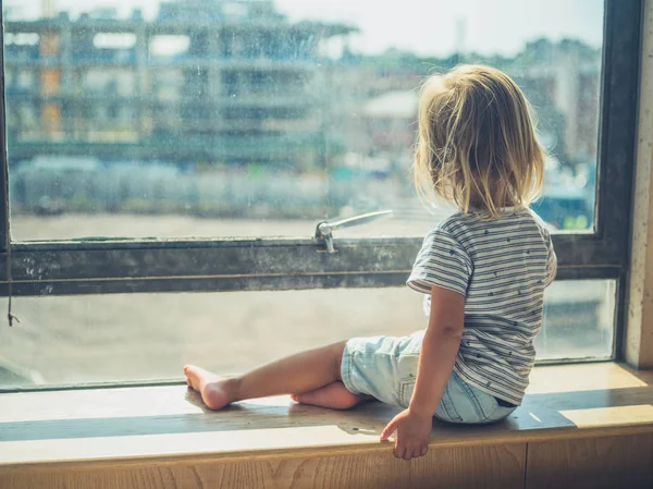 Little toddler sitting by the window in city aparetment — Stock Photo, Image