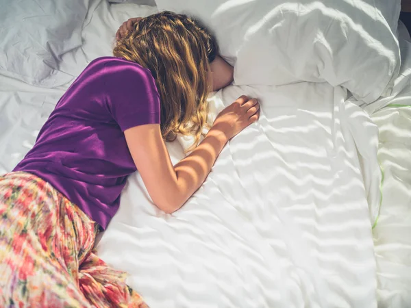 Junge Frau liegt an sonnigem Tag im Bett — Stockfoto