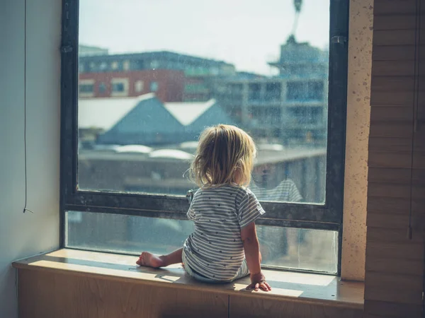 Little toddler sitting by the window in city aparetment — Stock Photo, Image